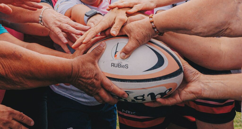 Players hands united around the official Les RUBieS Rugby Santé ball